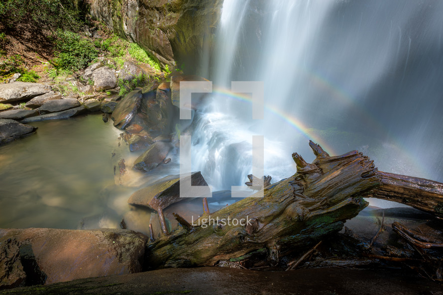 Double rainbow over silky effect slow shutter speed waterfall with fallen tree log