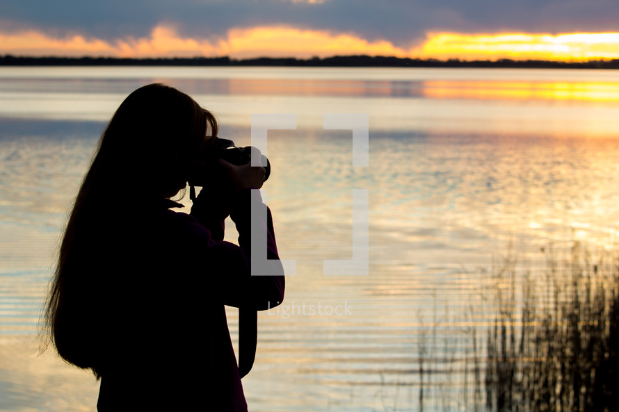a woman talking a picture of a lake at sunset 