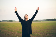 A man standing in a field with his hands raised in praise to the Lord 