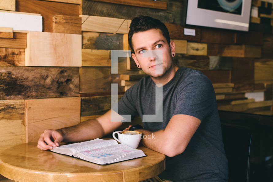 A man sits at a table with an open Bible and cup of coffee.