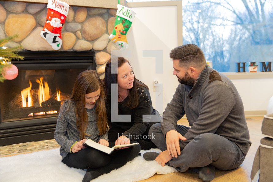 family reading a Bible in front of a fireplace at Christmas 