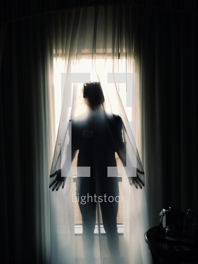 a woman standing behind a sheer curtain 