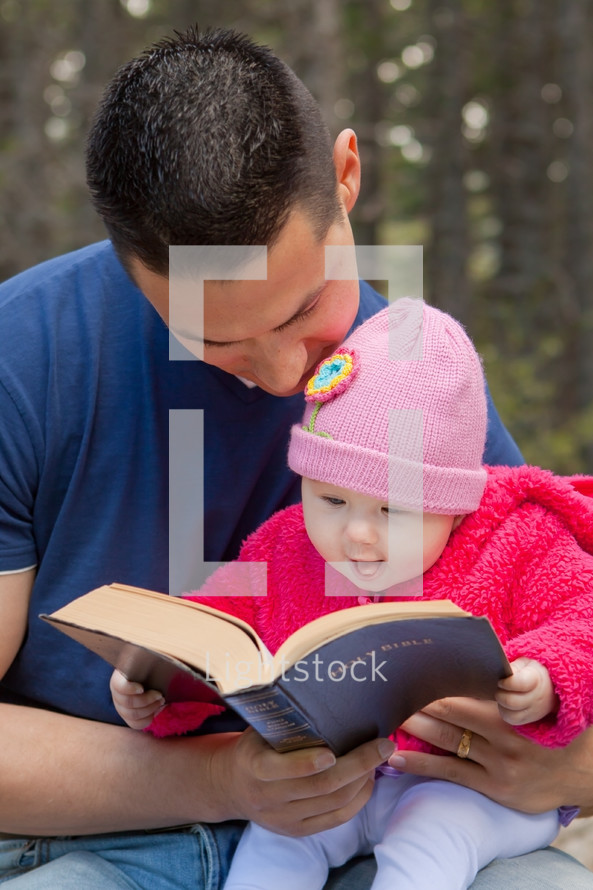 Father and infant daughter reading the Bible outdoors.