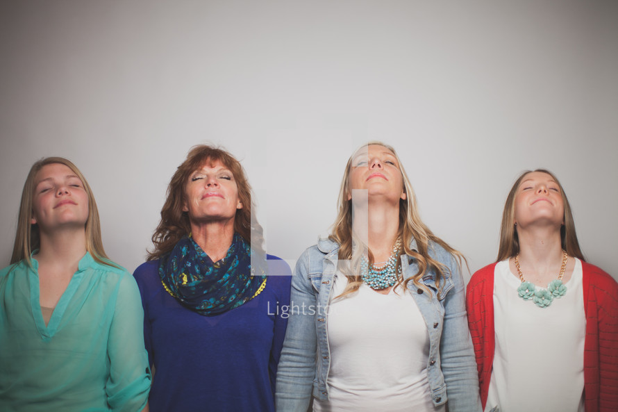 Mother and daughters with heads raised in prayer.