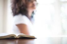 open Bible and a blurry image of a woman in the background