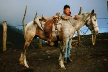 A boy stands next to his horse in the countryside.