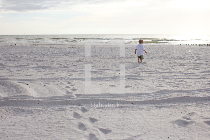 Toddler boy walking on a white sandy beach