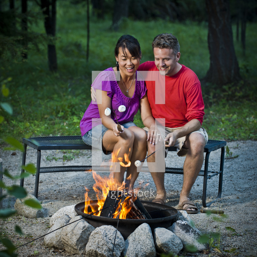 couple roasting marshmallows over a fire 