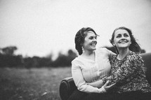 Smiling mother and daughter embracing while sitting on a couch in a field.