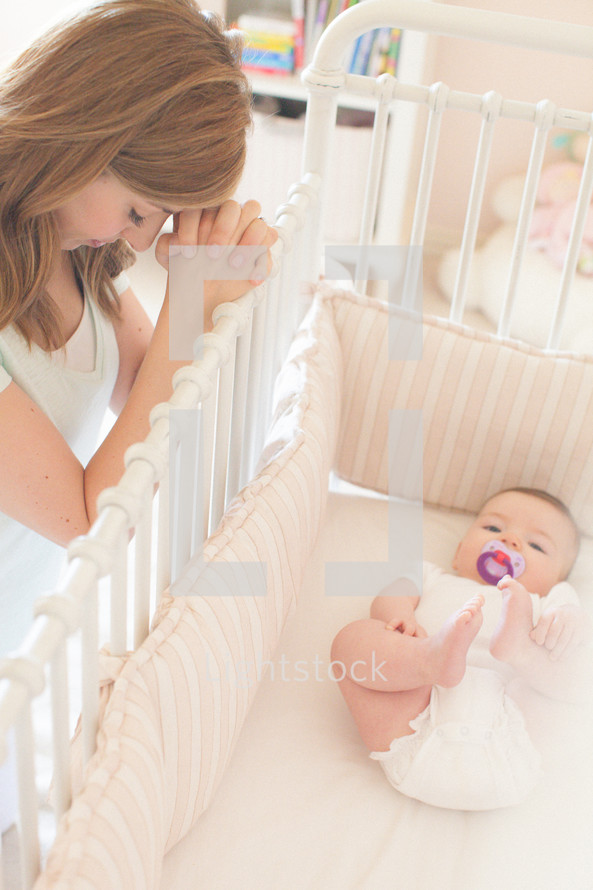 mother praying next to a baby in a baby crib