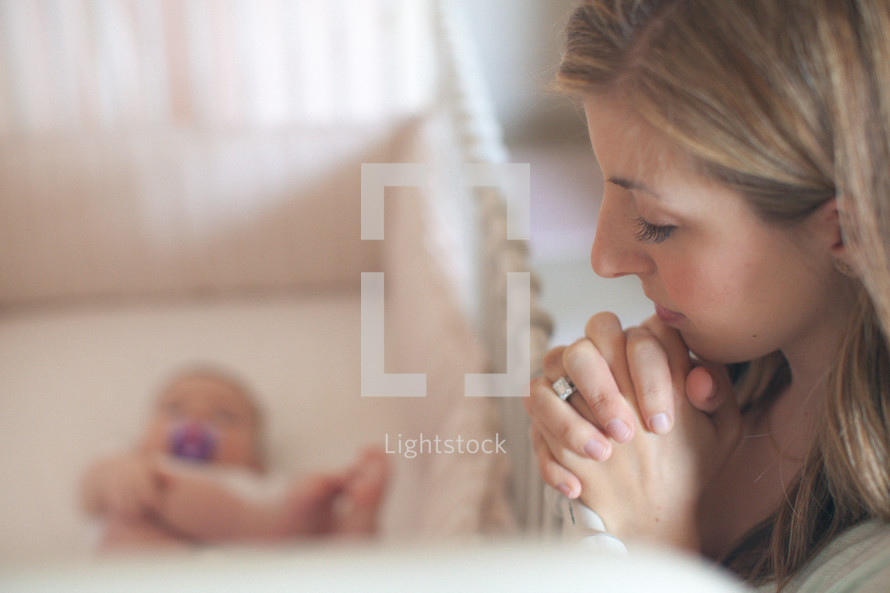 mother praying over a baby in a crib