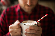 a man in a plaid shirt holding a mug of hot cocoa 