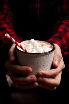 a man in a plaid shirt holdig a mug of hot chocolate