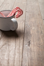 candy canes in a mug on a wood floor 