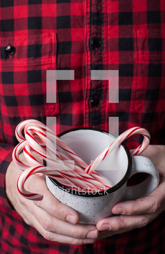 man in a plaid shirt holding a mug of candy canes 