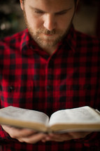 a man in a plaid shirt reading a Bible 