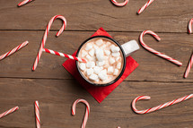 candy canes spread out on a wood table and a mug of hot cocoa 