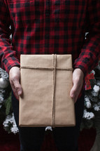 man in a plaid shirt holding a wrapped gift 