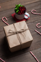mug with bows, wrapped gift, and candy canes spread out on a wood floor 