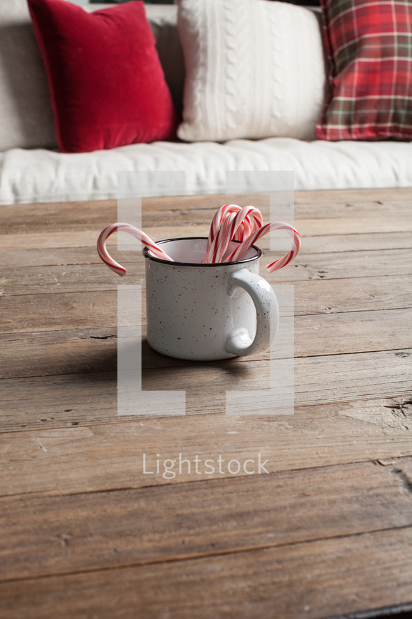 red and white pillows on a couch and candy canes in a mug on a wood table 