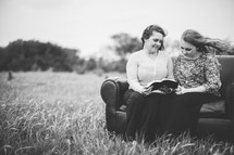 mother and adult daughter reading a bible together on a couch in a field