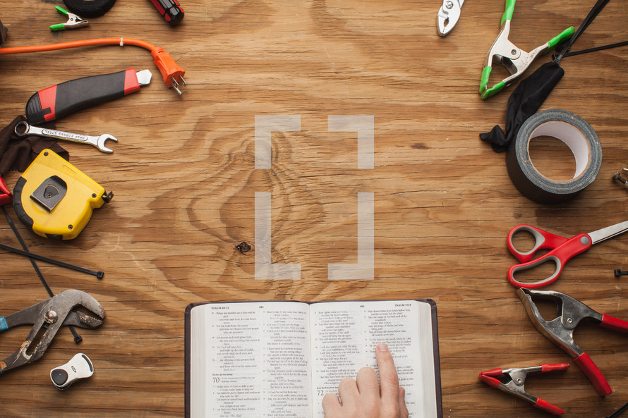 man pointing to a Bible surrounded by tools 