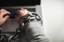 man bound in chains on a laptop keyboard 