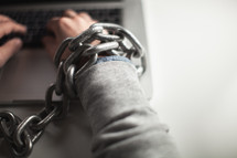 Wrists bound with chain working on a laptop computer.