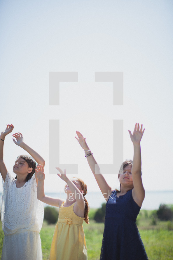young girls with hands raised in worship to God standing outdoors 