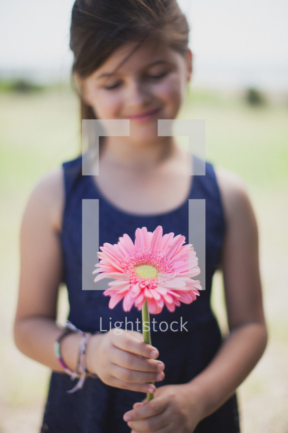 Smiling girl holding a flower outside.