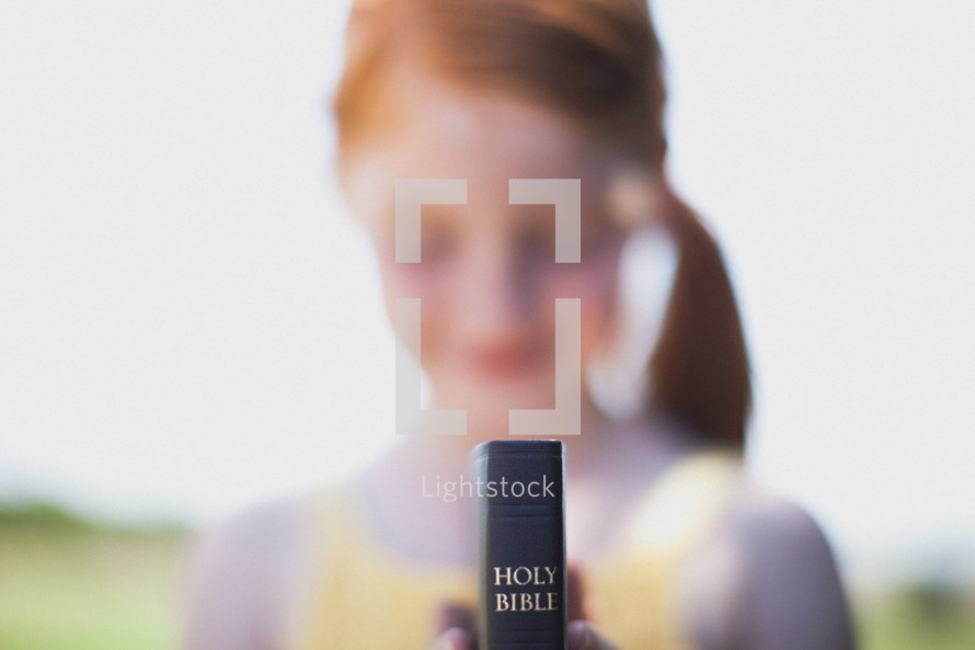 Girl standing outside holding a Bible.