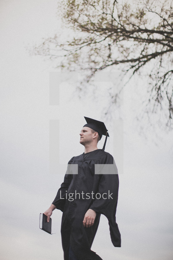 Graduate walking with Bible, looking in to the distance.