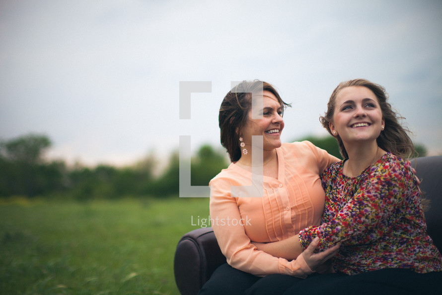 SMiling motehr and daughter embracing while sitting on a sofa in a field.