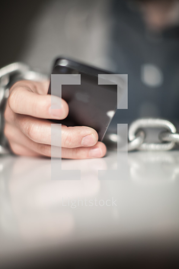 Wrists bound with chain holding a cell phone.