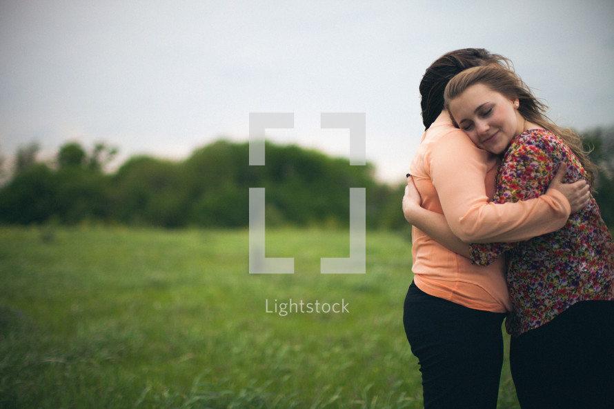 Mother and daughter embracing in a field.