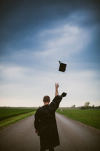 Graduate tossing cap while standing in the middle of the road.