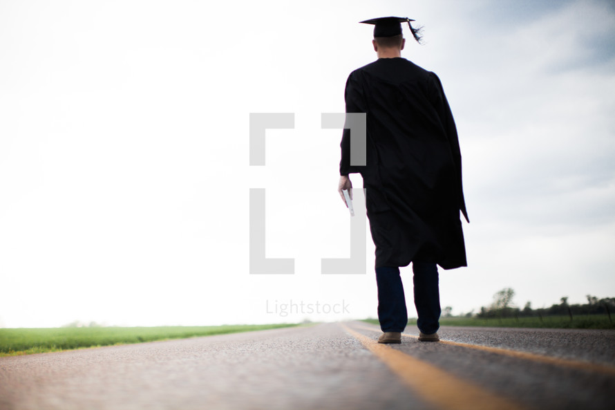 Graduate holding a Bible walking down the middle of the road.