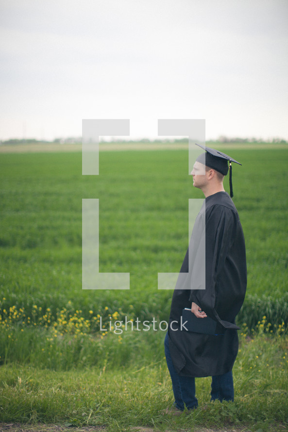 Graduate holding Bible in a field of green grass.