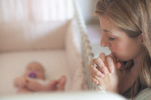 mother praying over a baby in a crib