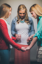 Mother and daughters holding hand sin a prayer circle.