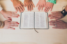 hands of diversity around an open Bible 