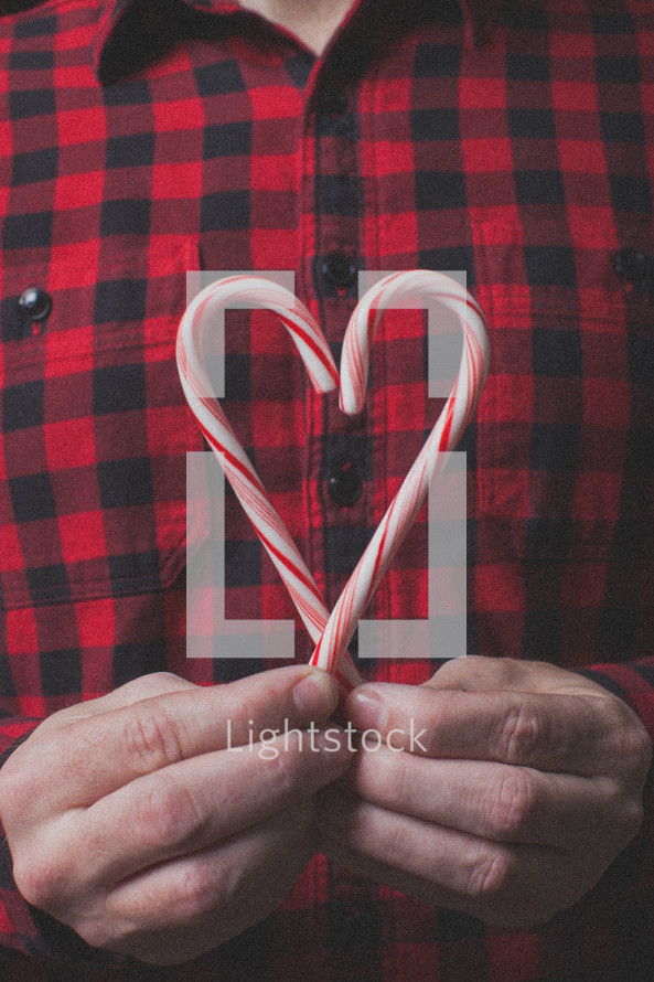 man in a plaid shirt holding a candy cane in the shape of a heart 
