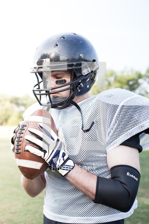 football player holding a football praying 