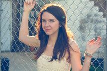 portrait of a young woman hanging on a chain linked fence 