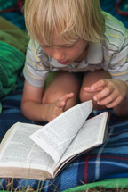 child reading a Bible in a tent and sleeping bag