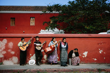 A mariachi band standing against a red stucco wall.