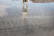 Reflection of a boy walking in the water on the beach.