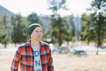 man standing outdoors in a wool cap and plaid shirt 