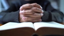Close up hands praying on Bible at wooden table in morning, Christian concept, zooming the camera out, away from hands