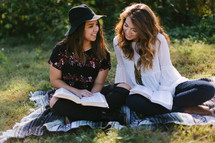 teen girls reading Bibles while sitting on a blanket outdoors 